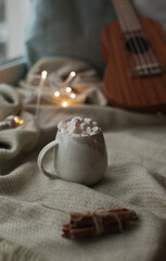 Hot cocoa with marshmallows and cinnamon sticks with christmas lights and guitar at night