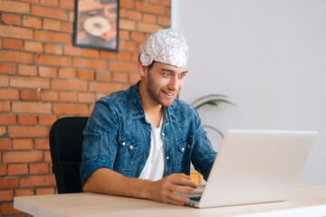 Medium shot of crazy male conspiracy theorist wearing aluminum foil protect brain watching shocked...