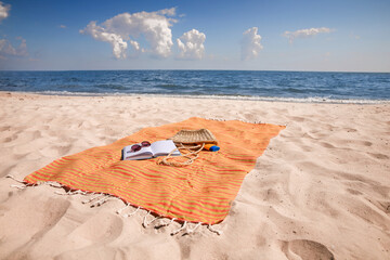 Orange striped beach towel with bag, accessories and book on sandy seashore
