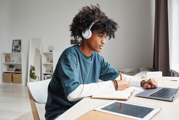 Side view portrait of African-American teenage boy studying at home or in college dorm and using...