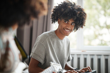 Portrait of young African-American musician composing music at home and using DJ keyboard, copy...