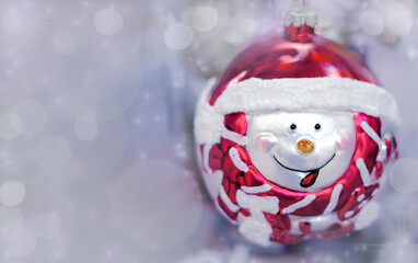 Obraz premium Christmas ball with smiling funny face on gray background with bokeh, copy space