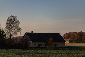 country house in Latvia in middle of agricultural field under blue sky. Sunset evening light