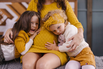Children hugs mom's pregnant belly. Happy parenting. Expectation of the third child. The sister is...