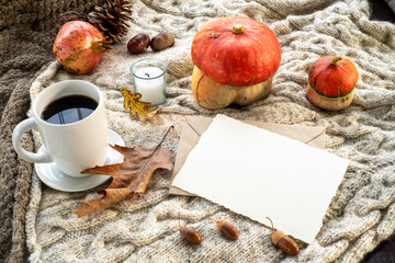 Cozy autumn breakfast scene. Blank greeting card mockup and envelope with cup of coffee or tea, candle, pomegranate, pumpkins.Plaid wool background.Fall, thanksgiving day, halloween concept.Top view