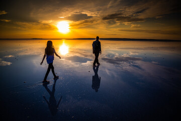 Mother and daughter walking on reflection salt lake at sunset