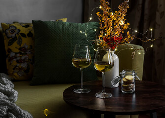 Cozy evening home interior - sofa, table with two glasses of white wine and a garland of dried...