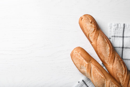 Tasty baguettes on white wooden table, flat lay. Space for text