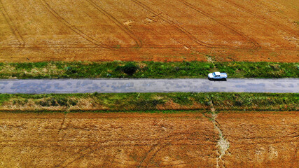 Pickup truck stands on a rural road between fields with wheat. View above from drone.