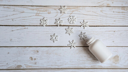 an open pill jar lies on a white wooden background and small white snowflakes pour out of it with a place for the text , the concept of Christmas