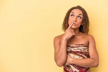 Young latin transsexual woman isolated on yellow background looking sideways with doubtful and skeptical expression.
