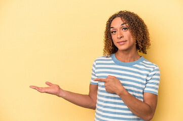 Young latin transsexual woman isolated on yellow background excited holding a copy space on palm.