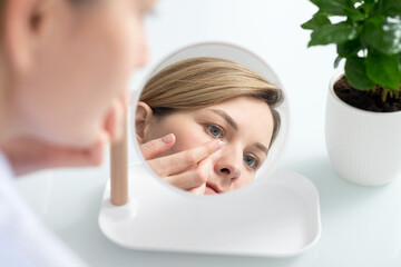 A woman sits in front of a mirror and puts contact lenses on her eyes