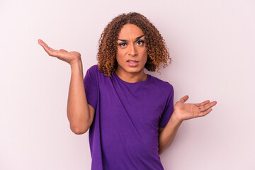 Young latin transsexual woman isolated on pink background confused and doubtful shrugging shoulders to hold a copy space.