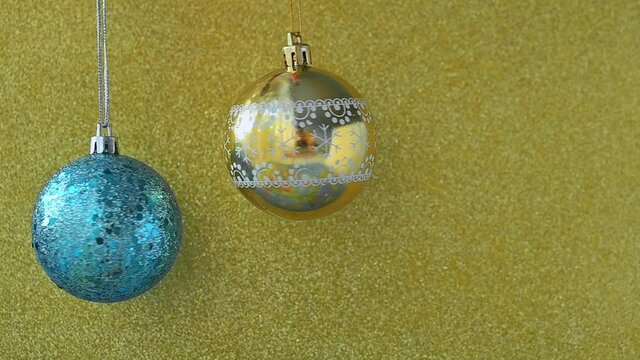 Merry Christmas and Happy New Year. Christmas gold and blue balls hanging on a string on a shimmering shiny gold background. Greeting card or banner for website sale. High quality FullHD footage
