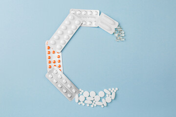 Letter C from medical pills, blisters, syringe and vaccine vial on blue background. Pharmaceutical alphabet. Complex therapy. 