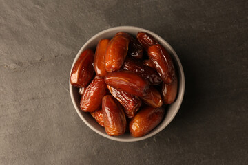 Tasty sweet dried dates in bowl on black table, top view