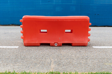Centered view of a bright orange water filled traffic barrier on an asphalt street before a fence...
