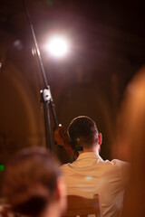 A view of a solo cello player in a white shirt from behind a symphony orchestra during a live...