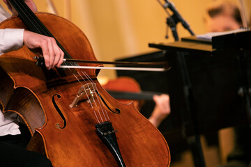 A musicians hand holding a bow and playing a cello during a rehearsal or a concert of a symphony orchestra