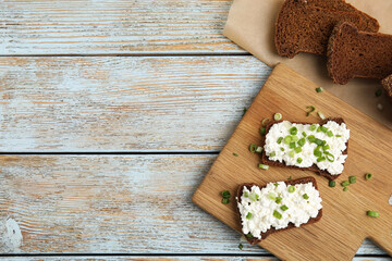 Bread with cottage cheese and green onion on light blue wooden table, flat lay. Space for text