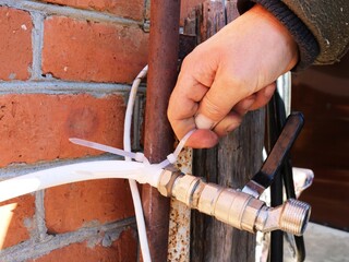 tightening a plastic clamp on a water pipe outside a brick building, installing a garden water tap, garden watering equipment in the process of reinstallation