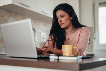 Beautiful young woman wearing a pajama and using a laptop while working from home