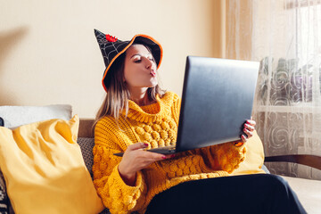 Halloween lockdown. Woman in witch hat sending kisses online in video chat on laptop. Holidays...