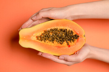 Papaya fruit on a orange background in woman hands. Tropical fruit.