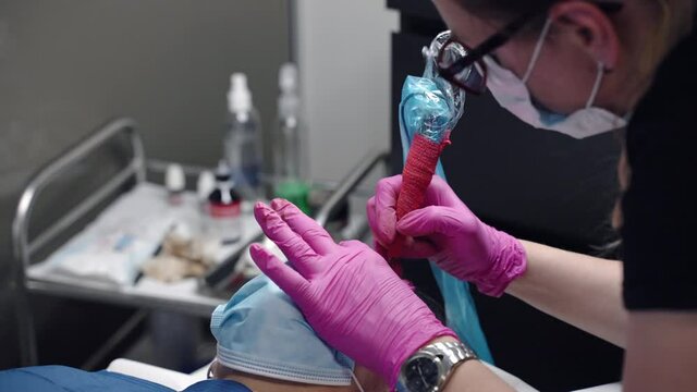 Microblading procedures in spa beauty salon, make up artist in protective pink gloves making permanent eyebrows tattoo with tattoo machine. Eyebrows correction, rejuvenate procedures