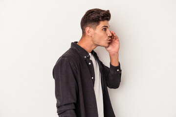 Young caucasian man isolated on white background is saying a secret hot braking news and looking...