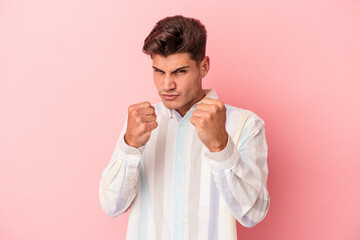 Young caucasian man isolated on pink background showing fist to camera, aggressive facial...