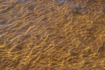 Transparent water in the river. Summer day clear water of light brown color from the sand at the bottom of the reservoir. The rays of the sun are reflected from the edges of the waves.
