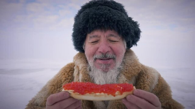 Front View Portrait Bearded Indigenous Old Man Holding Sandwich With Red Caviar Looking At Camera Smiling. Happy Positive Asian Northern Guy Posing With Healthful Delicacy On Snowy Winter Day Outdoors