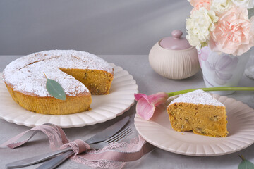 Obraz na płótnie Canvas Muffin or bundt cake decorated icing sugar on the plate with knife and fork on the granite table. Christmas Stollen traditional European festive dessert against vase with white and pink flowers. 