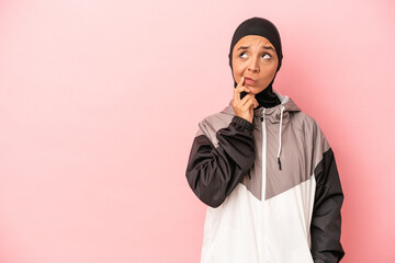 Young Arab woman with sport burqa isolated on pink background looking sideways with doubtful and skeptical expression.