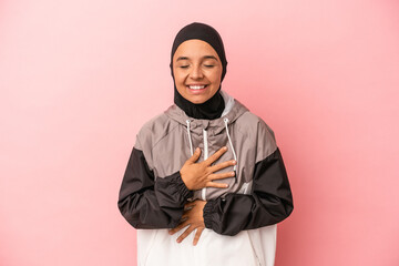 Young Arab woman with sport burqa isolated on pink background laughs happily and has fun keeping...