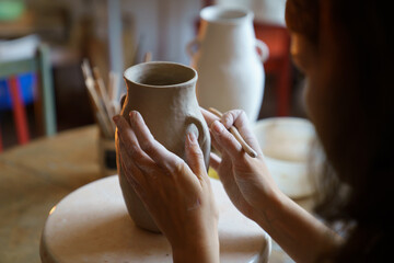 Creating potter tableware: cropped image of female ceramics artist molding clay jug in studio....