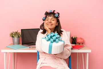 Obraz na płótnie Canvas Young mixed race woman with curlers holding cake isolated on pink background