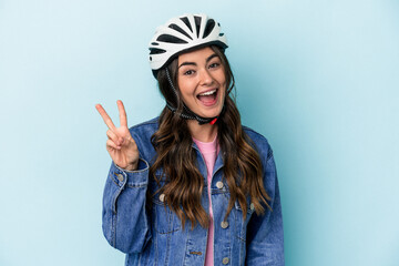 Young caucasian woman rinding a bike isolated on blue background joyful and carefree showing a peace symbol with fingers.