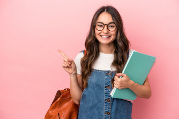 Young caucasian student woman isolated on pink background smiling and pointing aside, showing something at blank space.