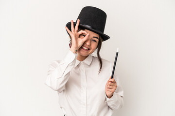 Young magician woman holding a wand isolated on white background excited keeping ok gesture on eye.