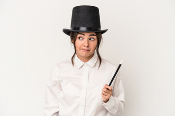 Young magician woman holding a wand isolated on white background confused, feels doubtful and unsure.