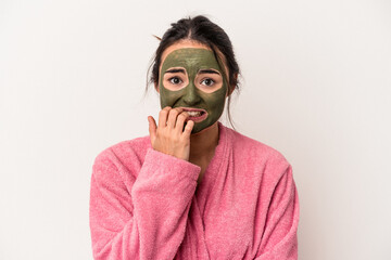 Young caucasian woman wearing a facial mask isolated on white background biting fingernails,...
