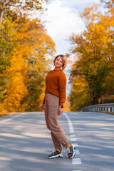 Fototapeta premium Smiling woman in a cozy sweater looks at the camera with her hands to the side an autumn forest