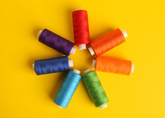 Different colorful sewing threads on yellow background, flat lay