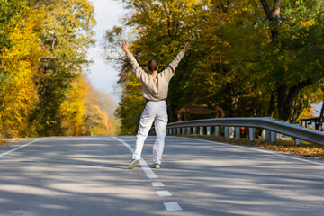 Back view of young woman standing walking in the autumn in the forest raises her hands up