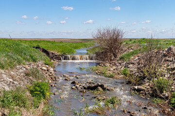 Water flowing through farm field in waterway. Concept of erosion control, drainage and water...