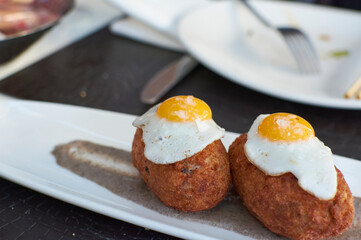 delicious homemade croquettes with shiny quail eggs on a gourmet sauce on a long tray, ready to be eaten in a pleasant evening.