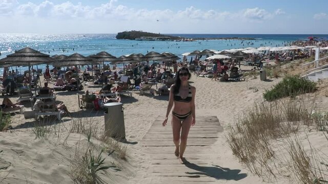 A pretty young brunette woman in a black and white swimsuit walks from the sea from the Nissi beach in Ayia Napa on the island of Cyprus